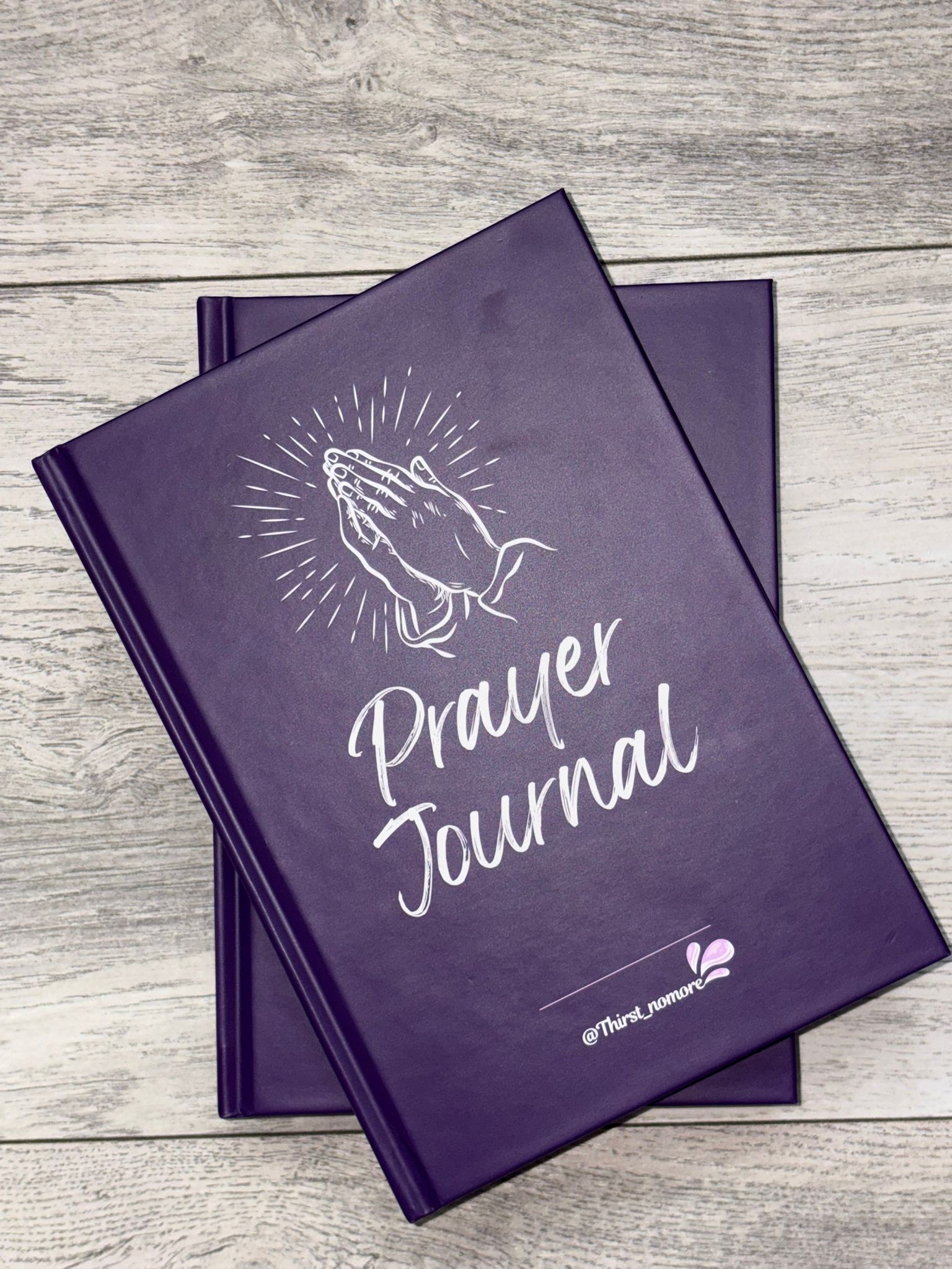 Purple prayer journal with praying hands illustration on a wooden surface