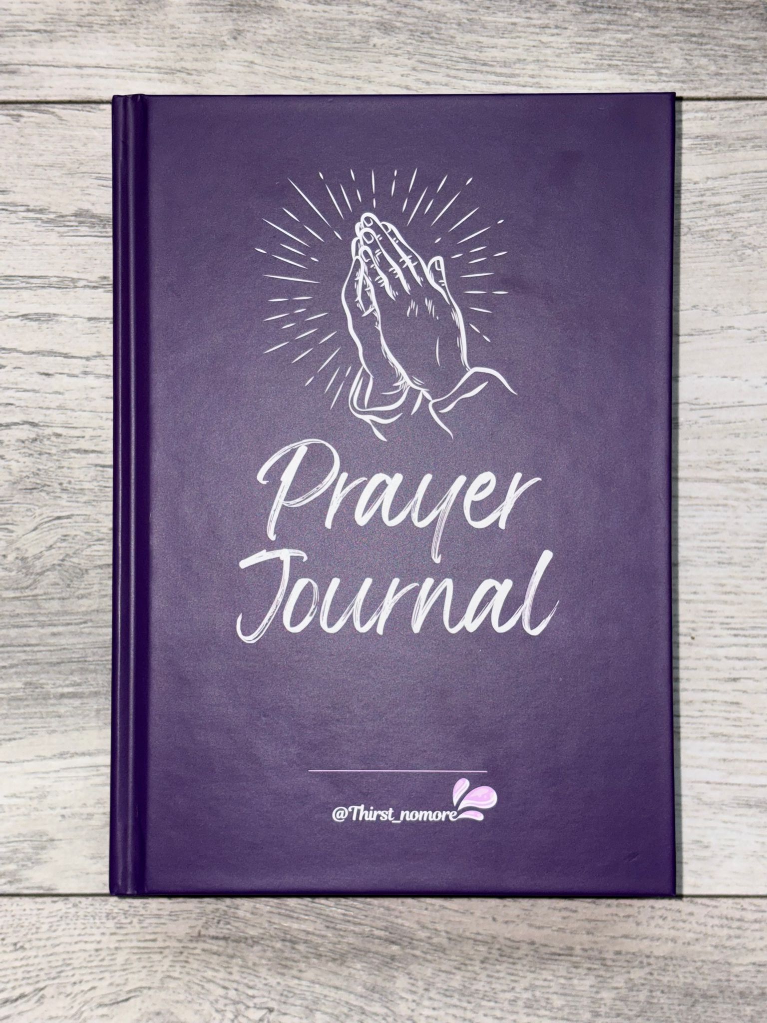 Purple hardback prayer journal with white text and design on a wooden surface