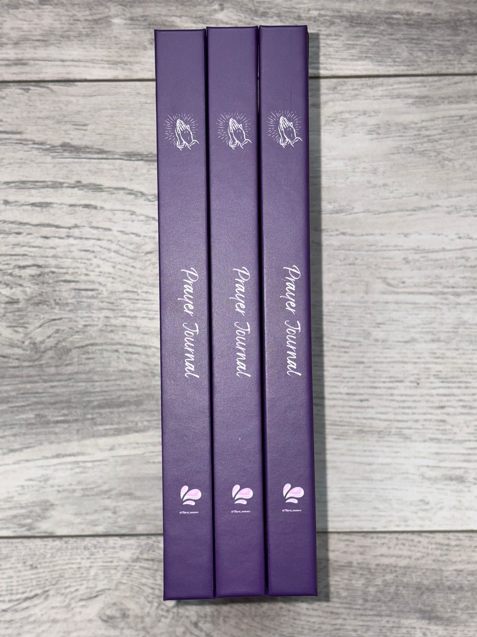 Three purple journals with a brand logo on a wooden surface